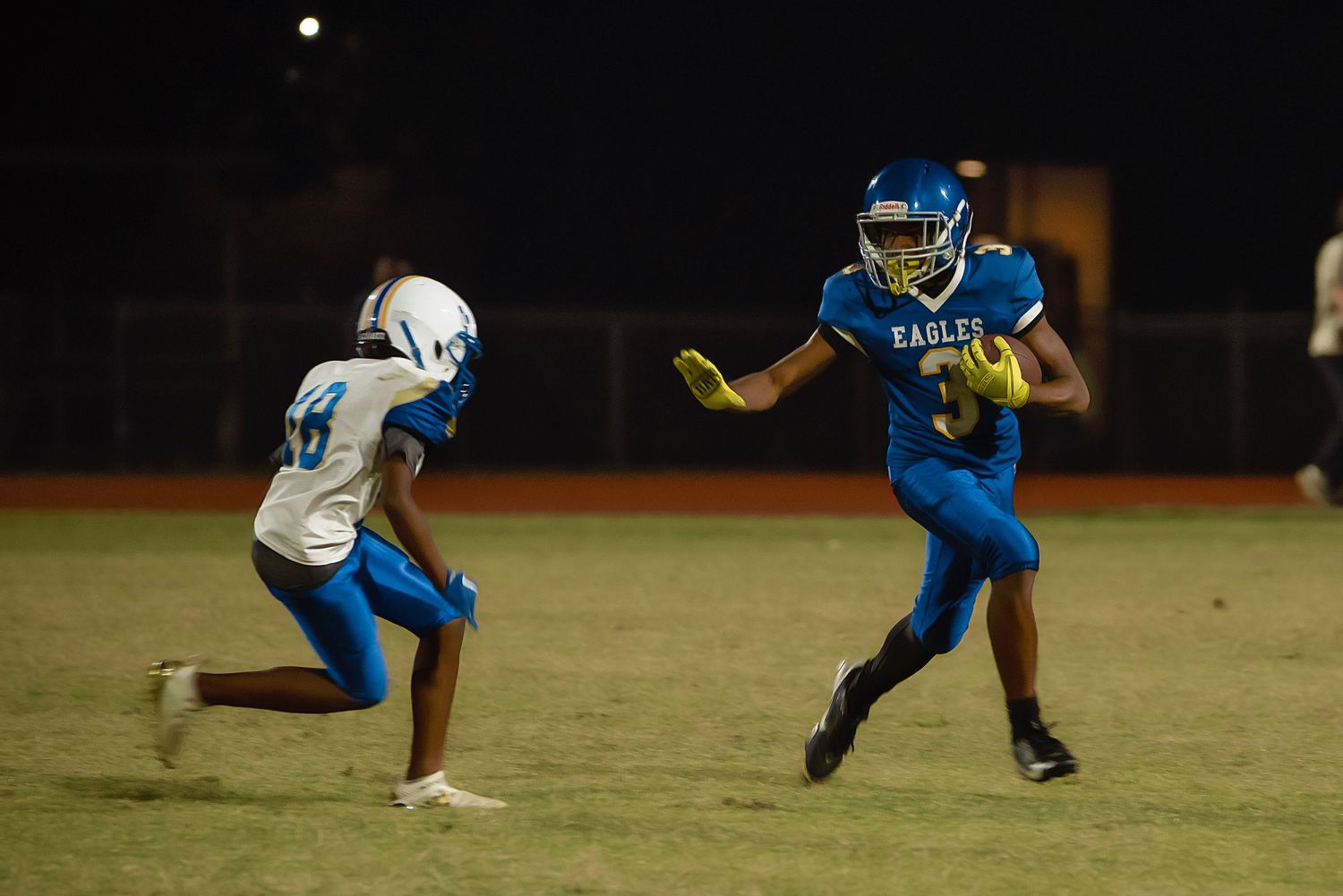 Football player in blue and yellow uniform makes diving catch attempt during nighttime game.