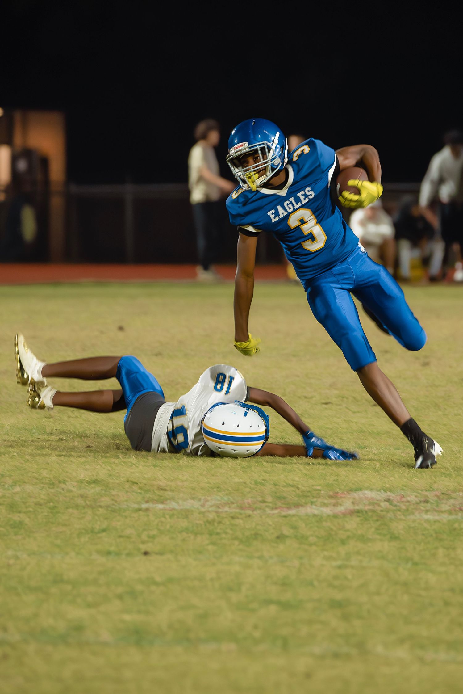 Football player in blue uniform falls forward onto grass field during athletic play.