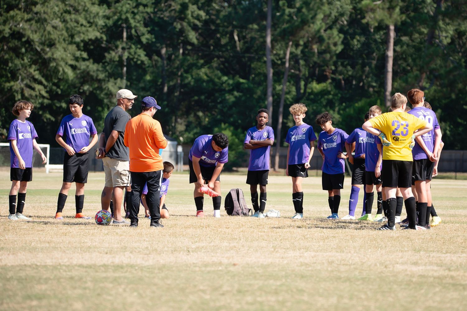 Soccer players line up on a grassy field during a team practice session in matching blue uniforms.