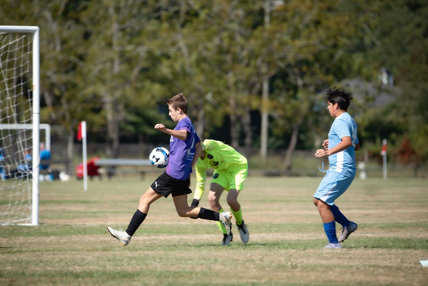 Soccer players compete for the ball during an outdoor match on a sunny day at a grass field.