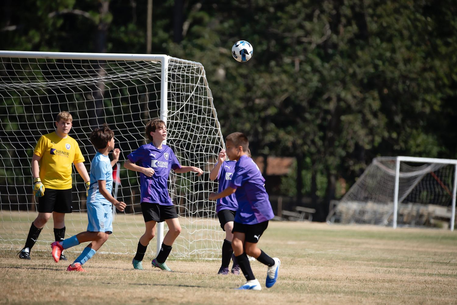 Soccer players battle for possession near a goal net during an outdoor match.