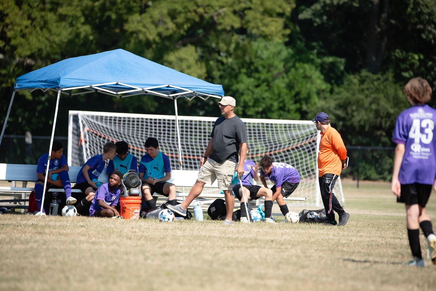 Youth soccer game underway with spectators watching from sideline tents on a grassy field.