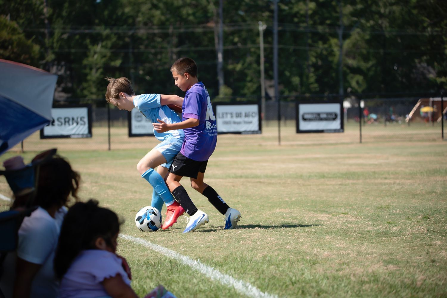 Players in blue and purple jerseys battle for possession during a soccer match on a grass pitch.