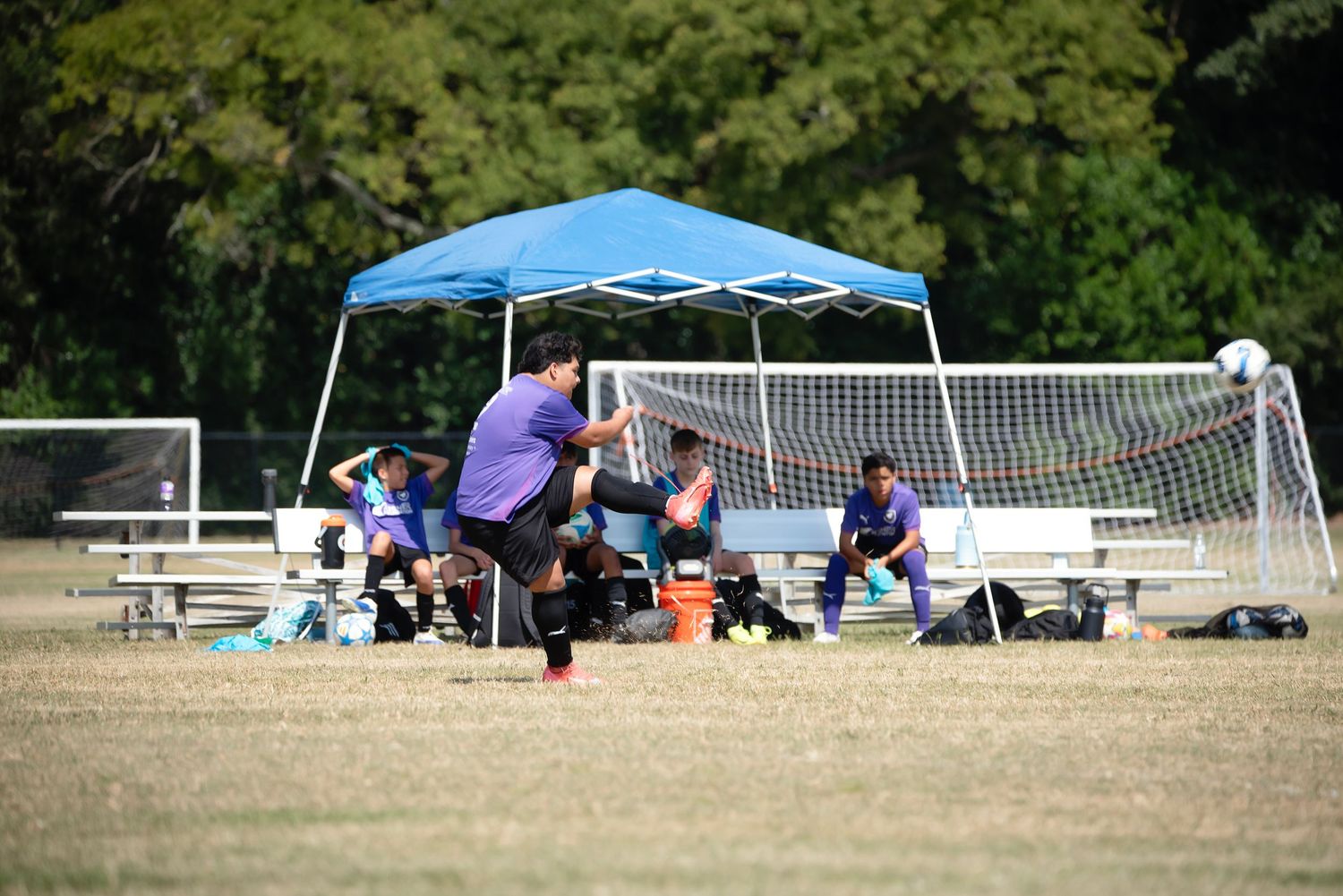 Wide view of soccer field showing goal posts, spectator tents, and benches during a match.