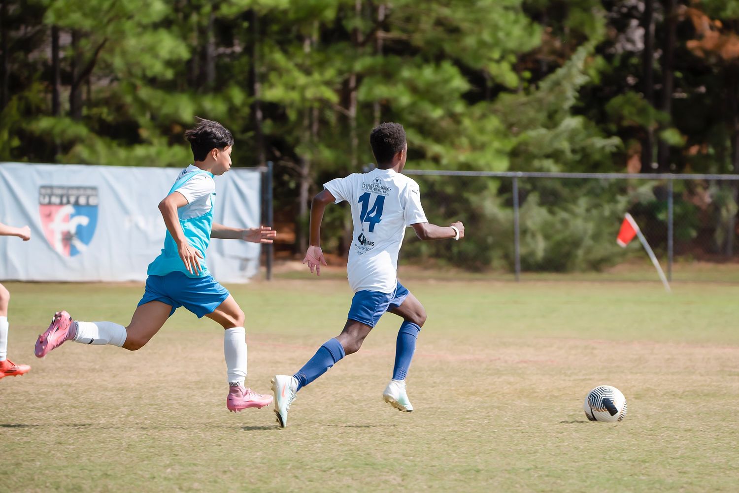 Two soccer players in white and blue uniforms battle for control of the ball during a match.
