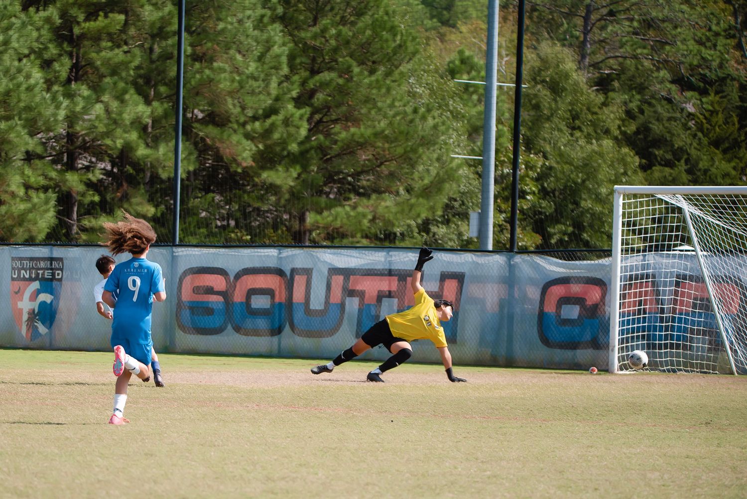 Wide view of a soccer field with players and goal posts during a youth game.