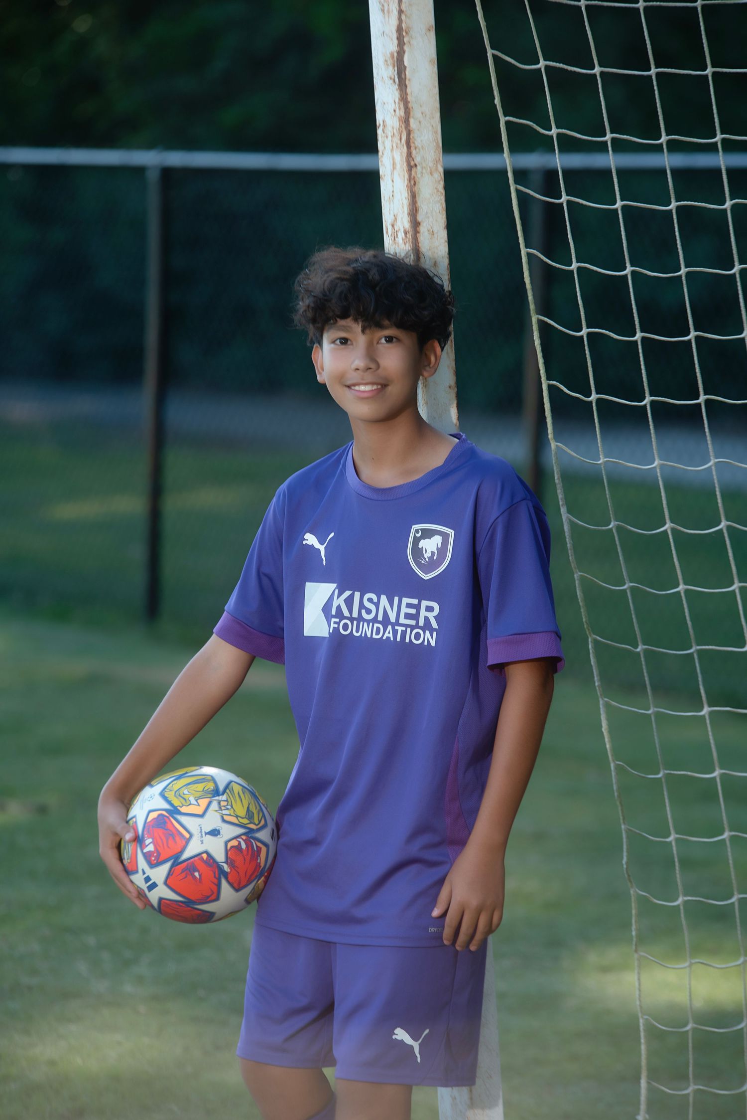 Young soccer players in purple uniforms practice near a goal net during an outdoor training session.