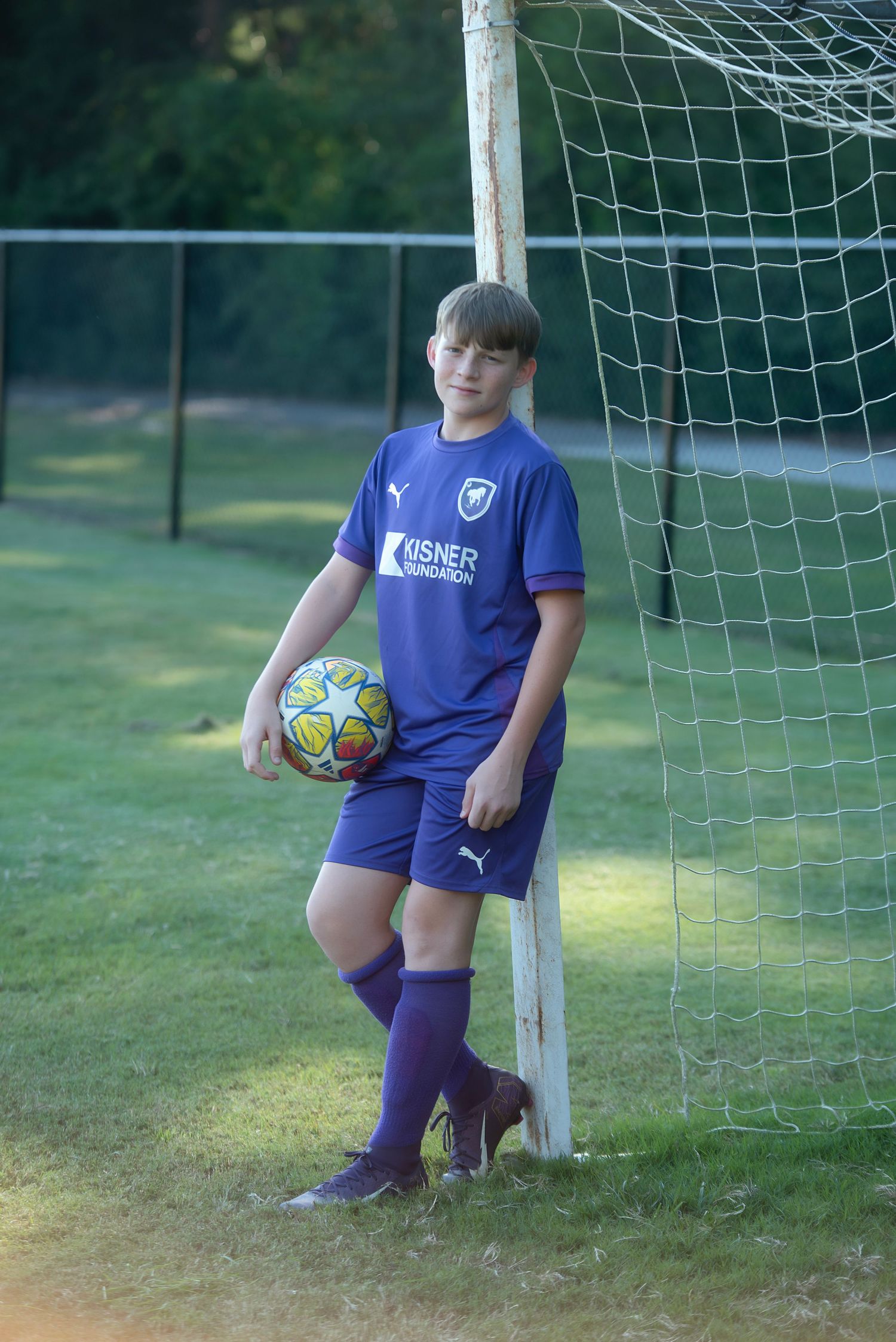 Soccer players in matching purple uniforms pose with bright soccer balls near a goal net.