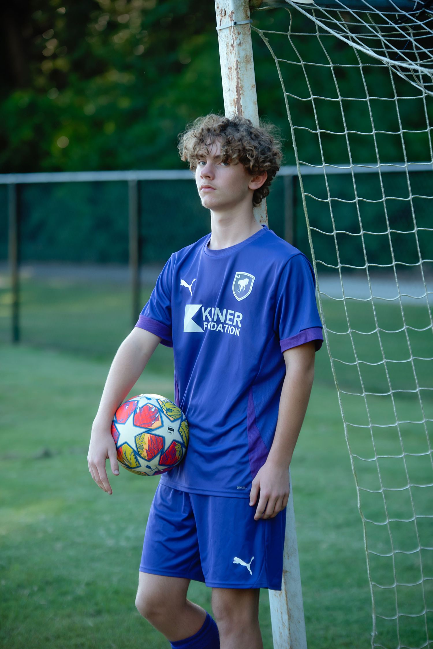 Players in purple Kisner soccer uniforms hold colorful soccer balls while posing by the goal.