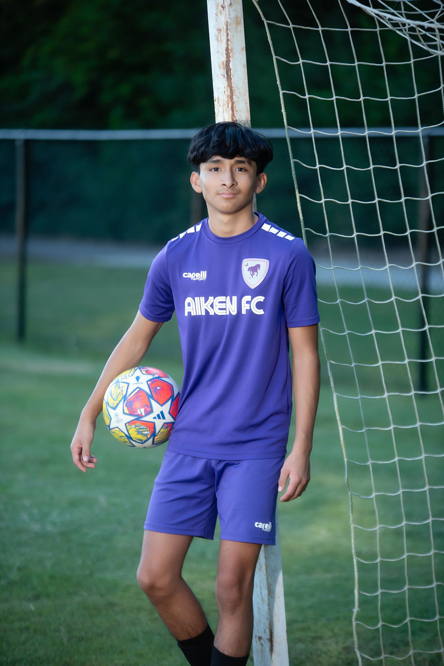 Youth soccer players in purple Aiken FC uniforms pose with colorful balls by the goal net.