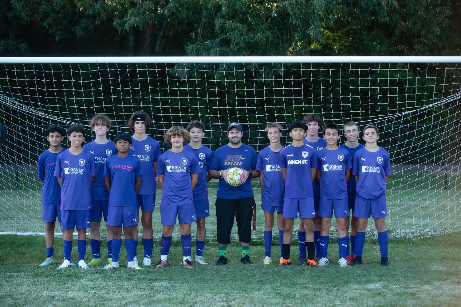 Youth soccer team in matching blue uniforms lined up in front of goal net on green grass field.