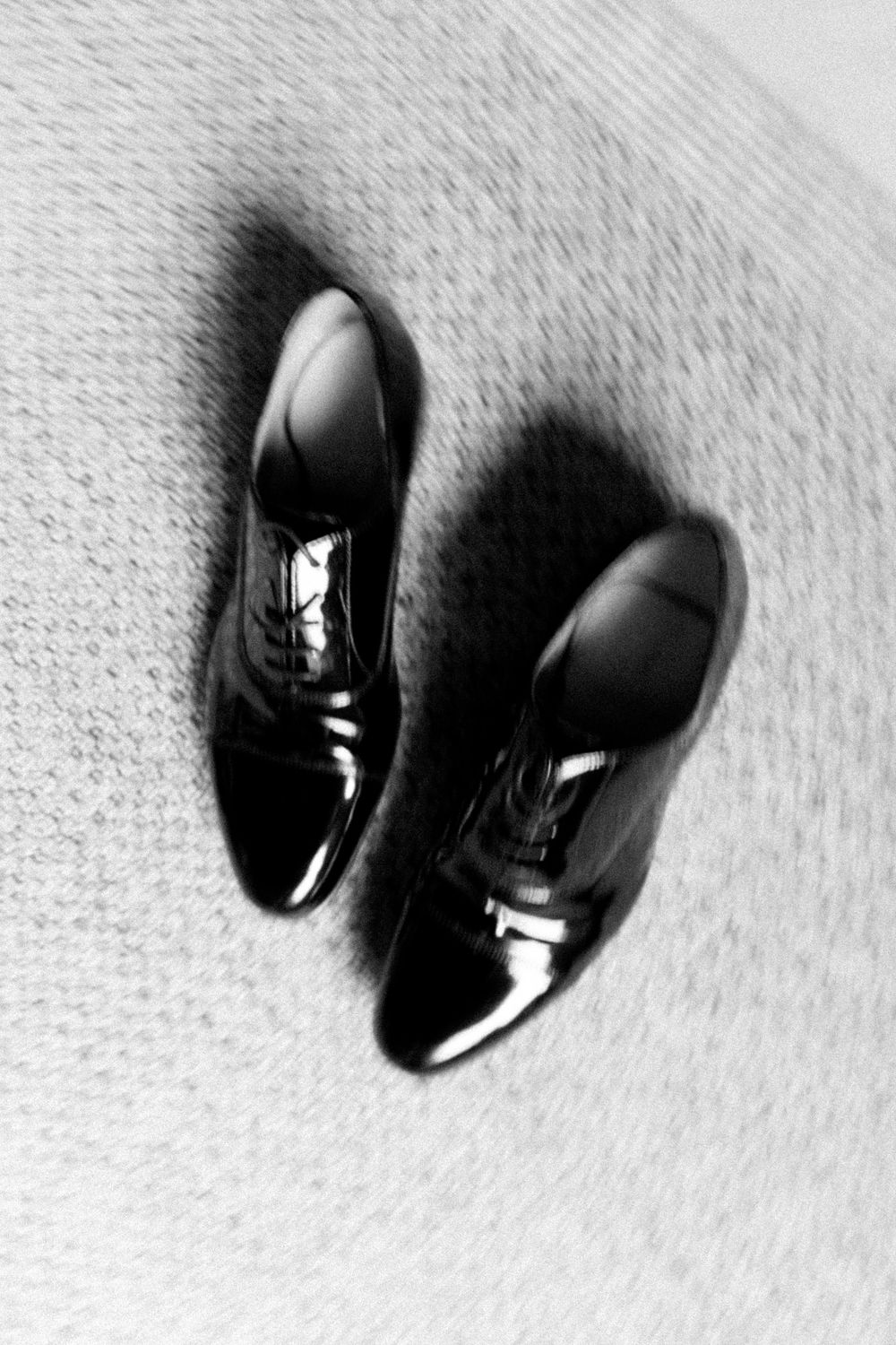 A series of black leather dress shoes photographed at different angles on a textured white background.