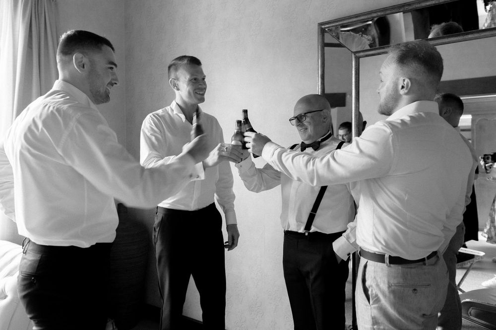 Black and white photo of men in white shirts toasting with bottles in an indoor setting.