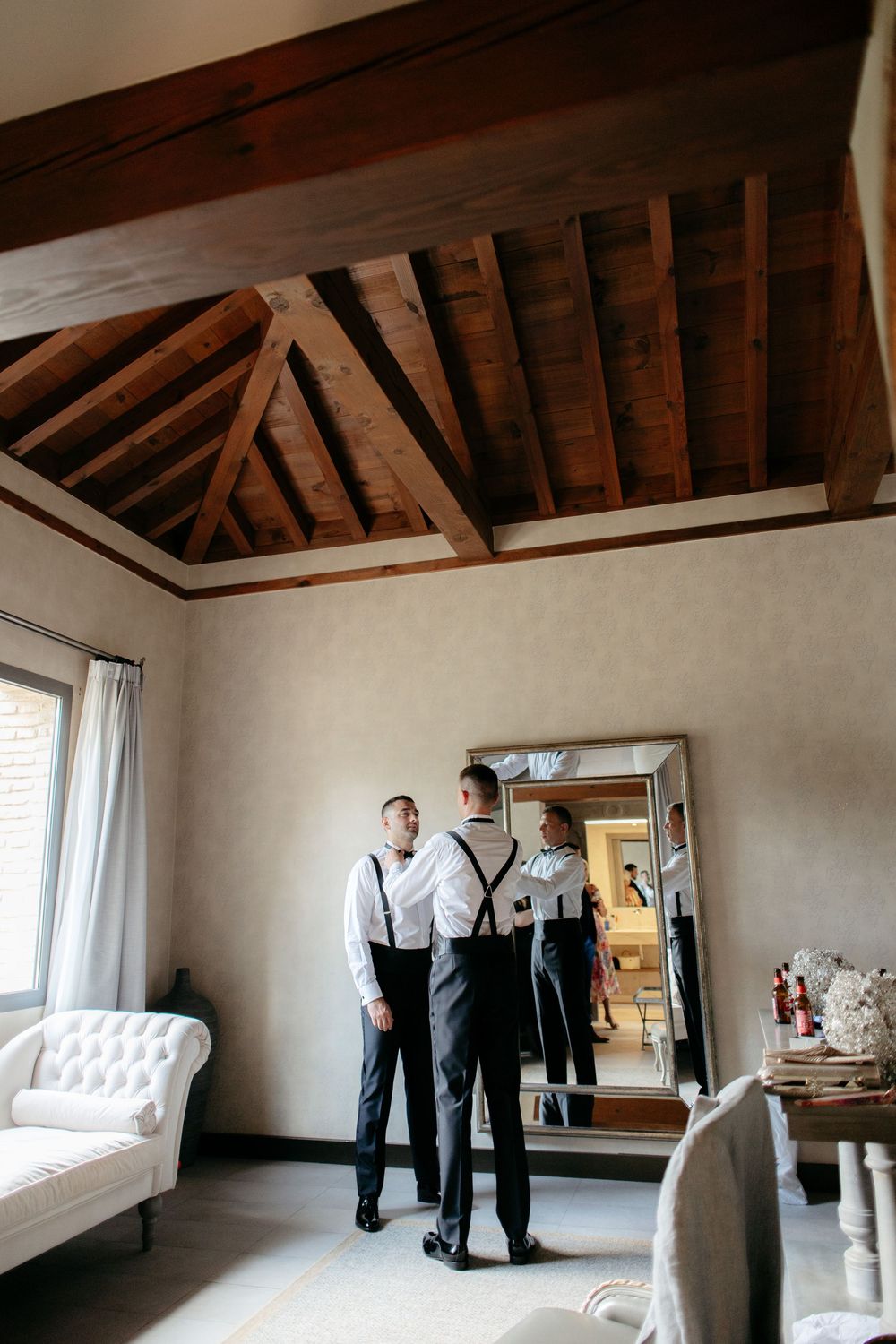 Elegant room with exposed wooden beam ceiling, white walls, and formal attire being prepared.