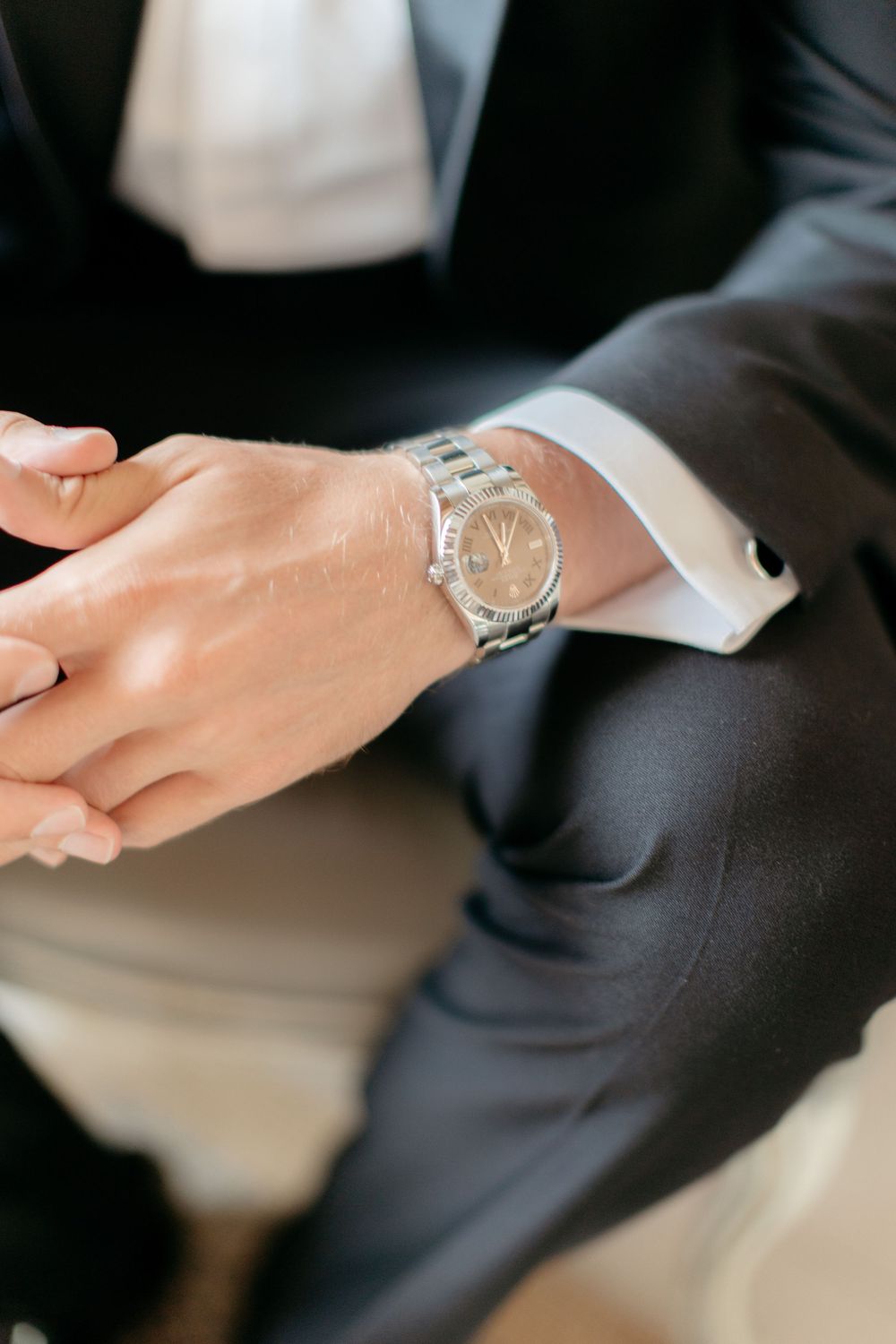 Close-up of hands wearing formal attire with a silver wristwatch visible.