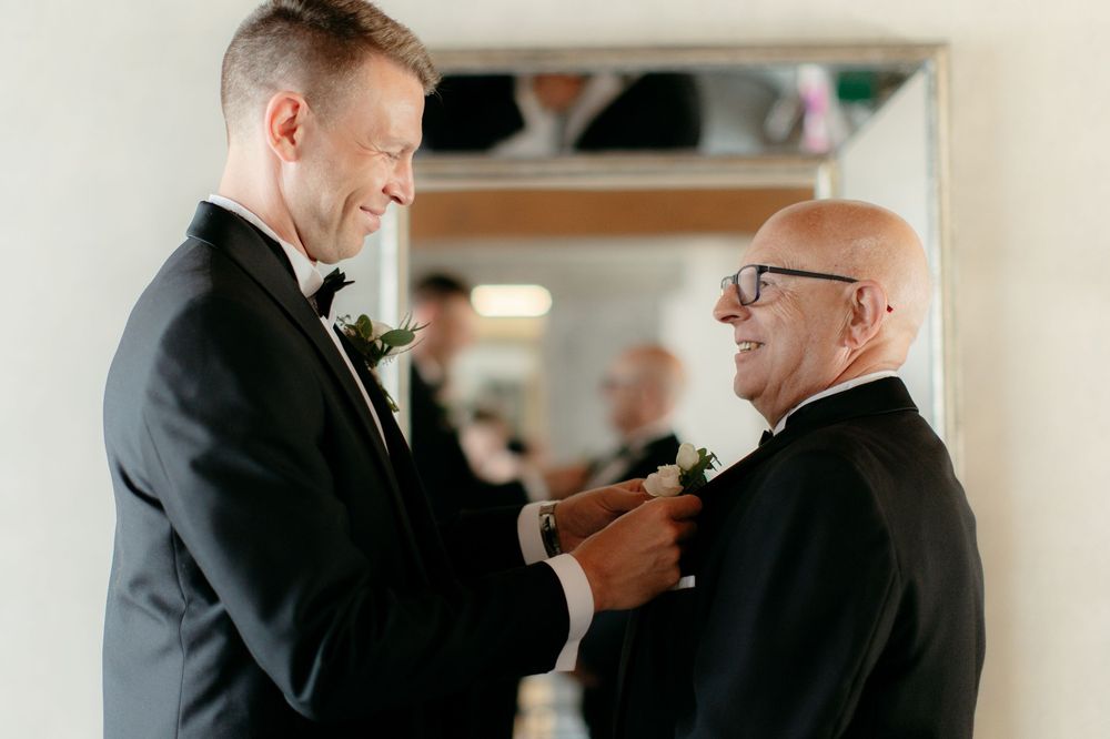 Two attendees share a heartfelt moment while adjusting formalwear before a ceremony.