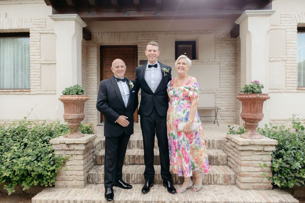 Three people stand together on a brick porch of a historic building with decorative planters.
