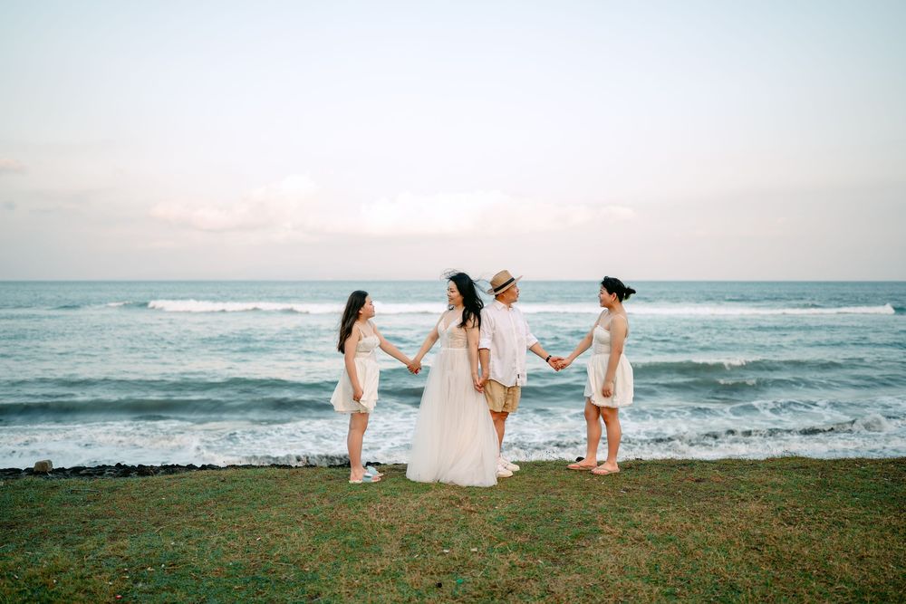 People in white dresses walking along a grassy oceanfront cliff at sunset.