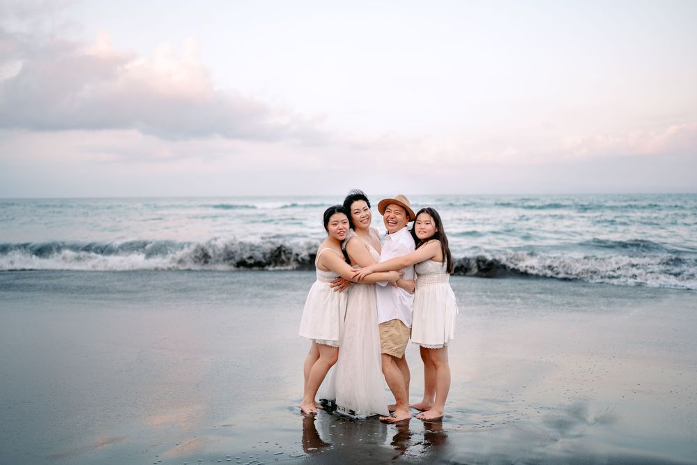 Group in white outfits posing together at sunset on a beach with ocean waves in the background.