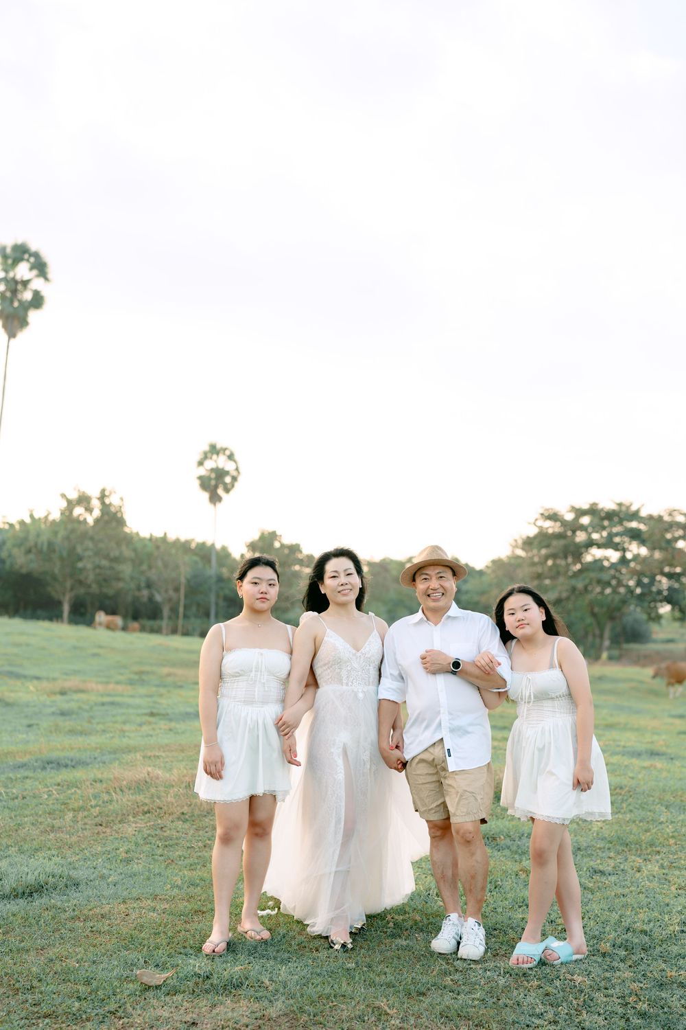Group wearing white outfits standing together in a grassy field with palm trees.