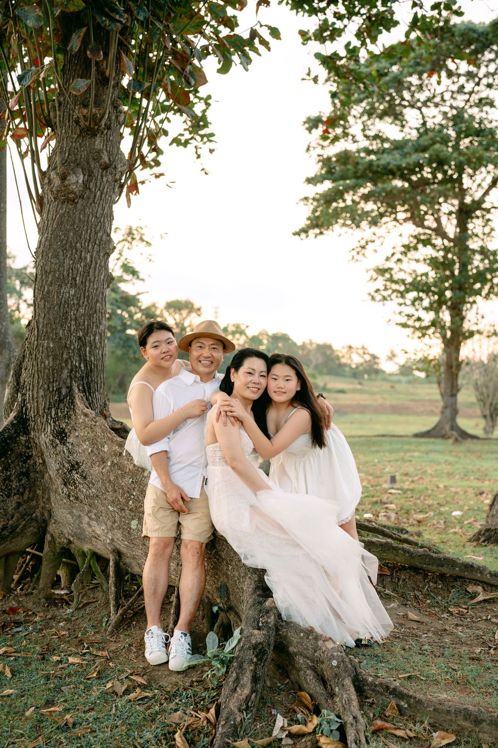 Group in white and beige outfits posing playfully around large tree trunks.
