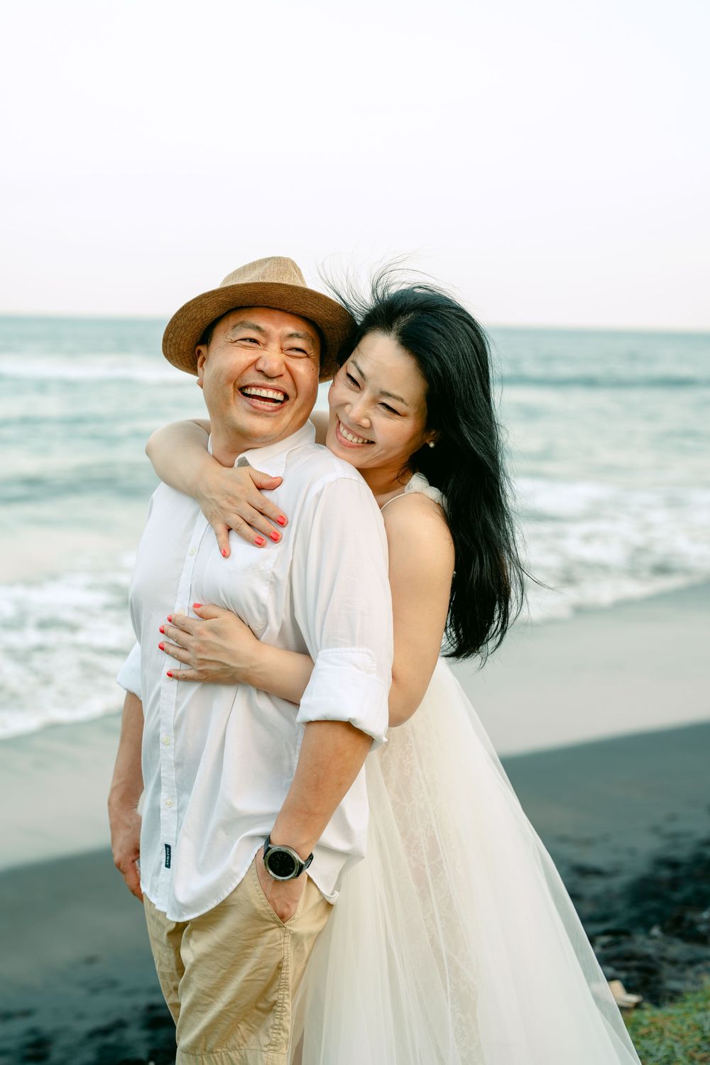 Joyful moment captured between people in white outfits embracing on a beach.