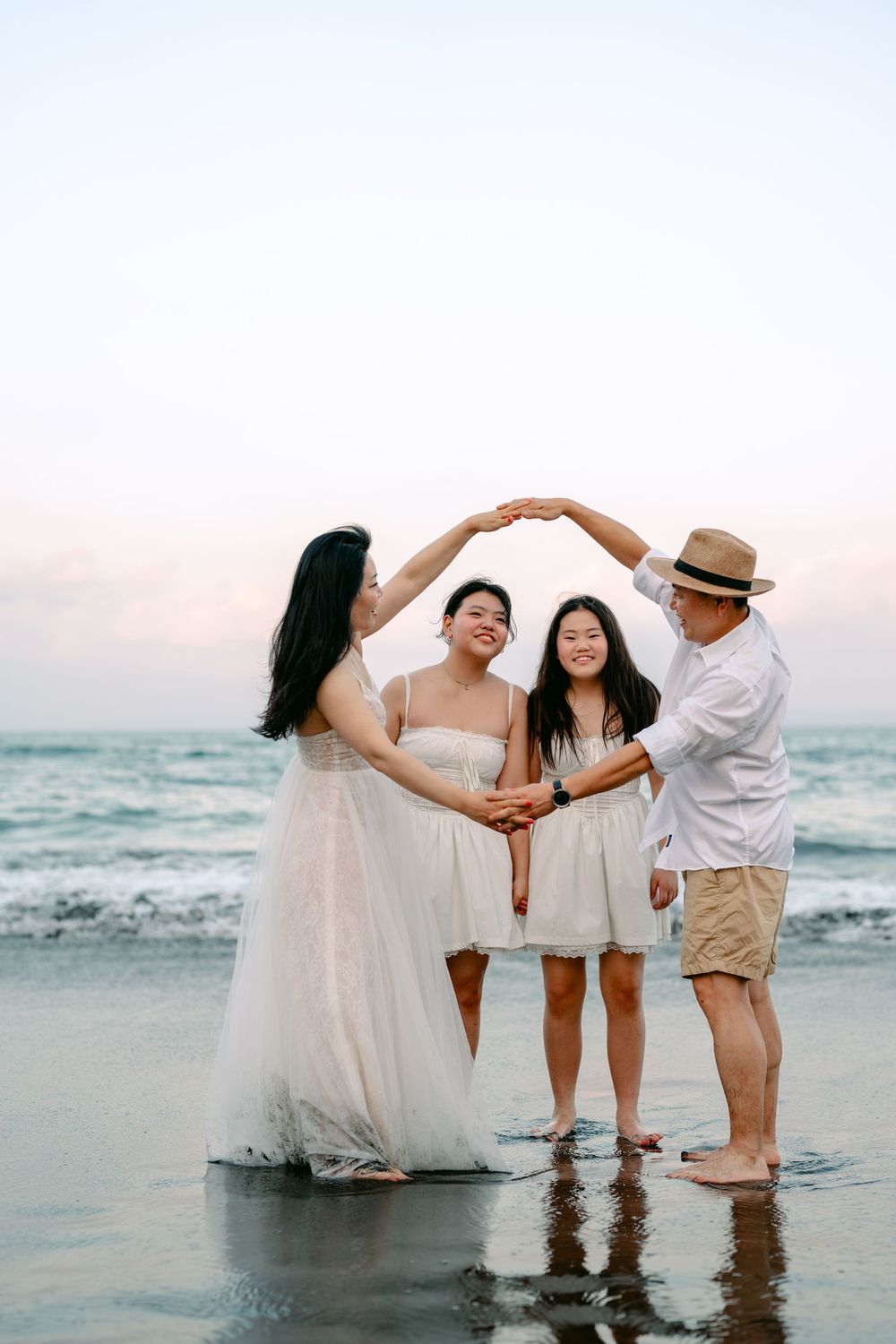 People in white outfits playing and dancing in shallow ocean water at sunset.