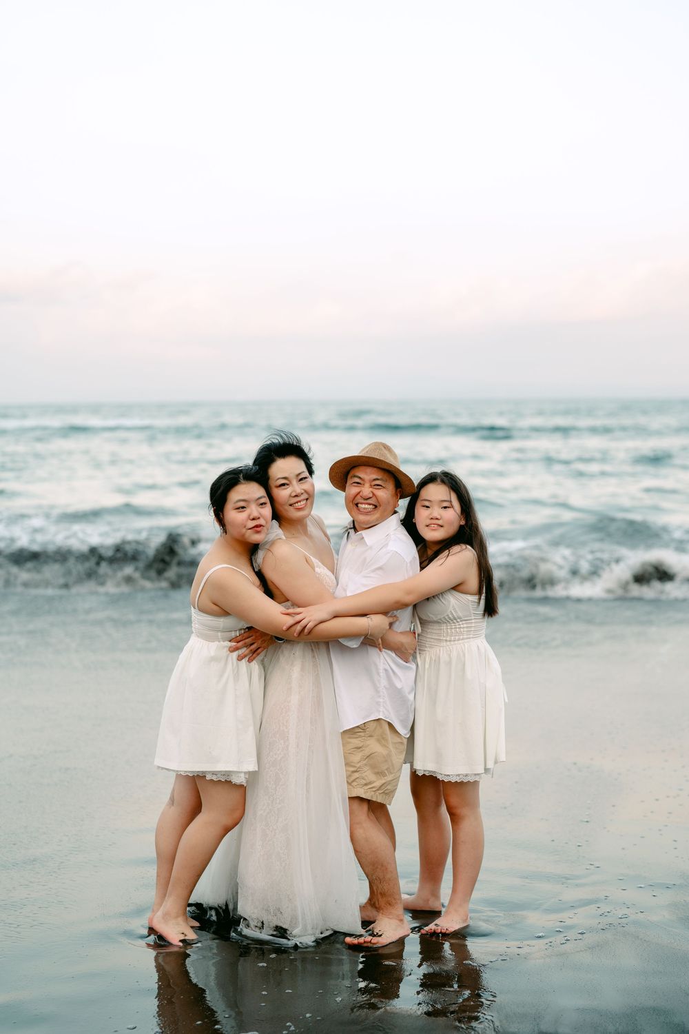 Group hug captured on beach with waves and sunset in background.