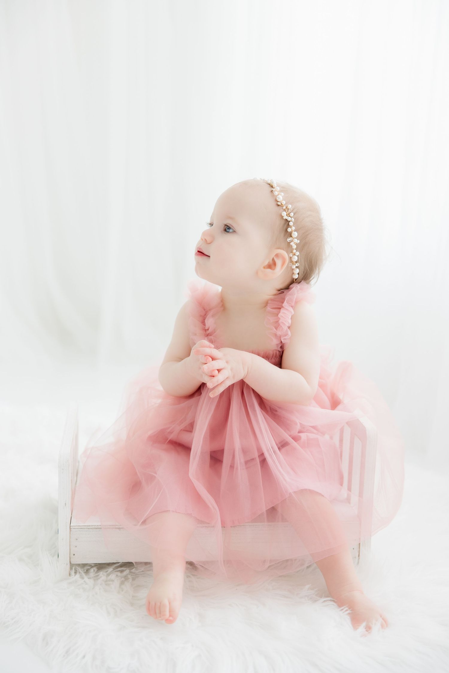 A baby wearing a pink tulle dress poses gracefully on a white backdrop in an ethereal photography session.
