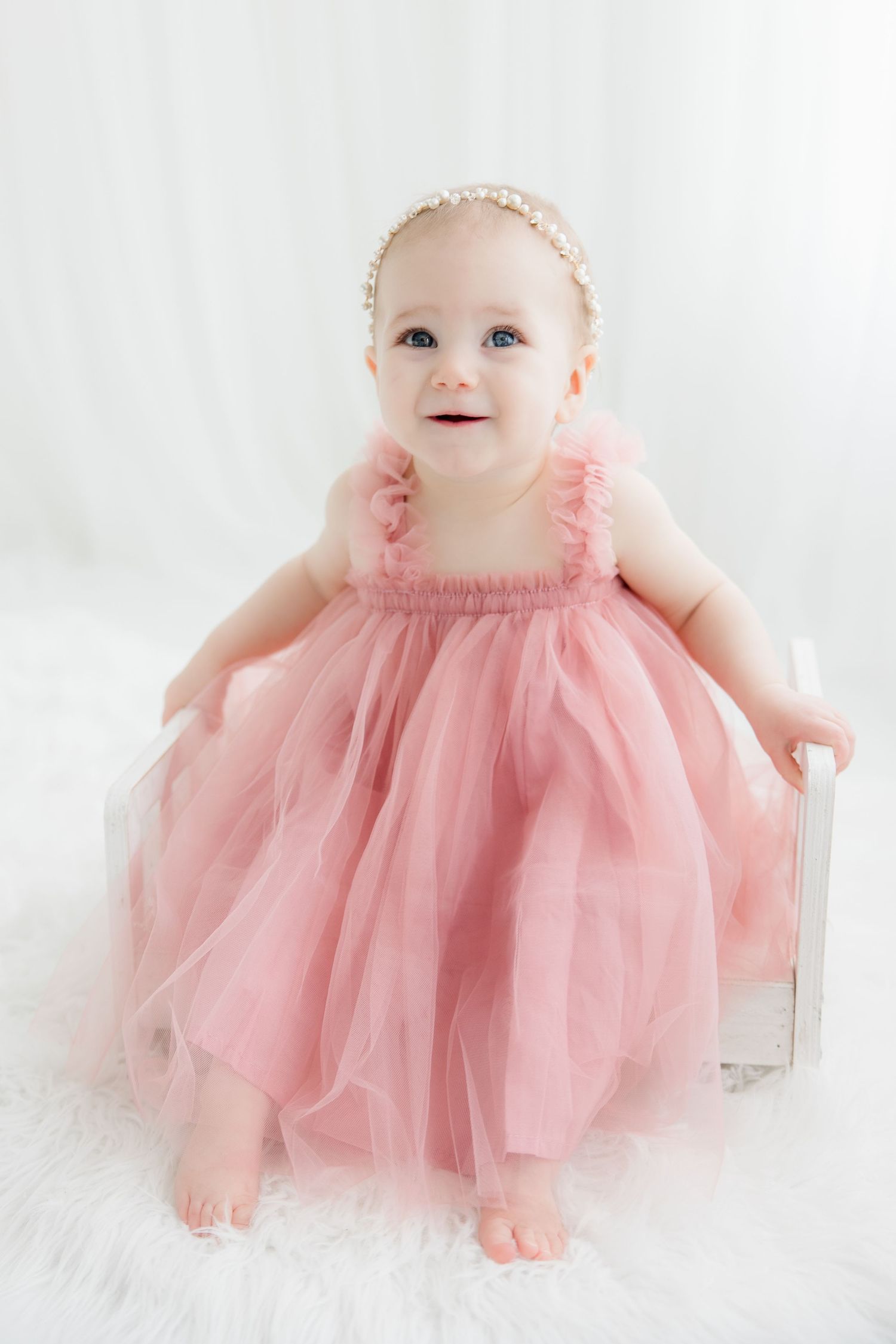 Baby wearing a pink tulle dress photographed on white backdrop in sweet milestone portraits.