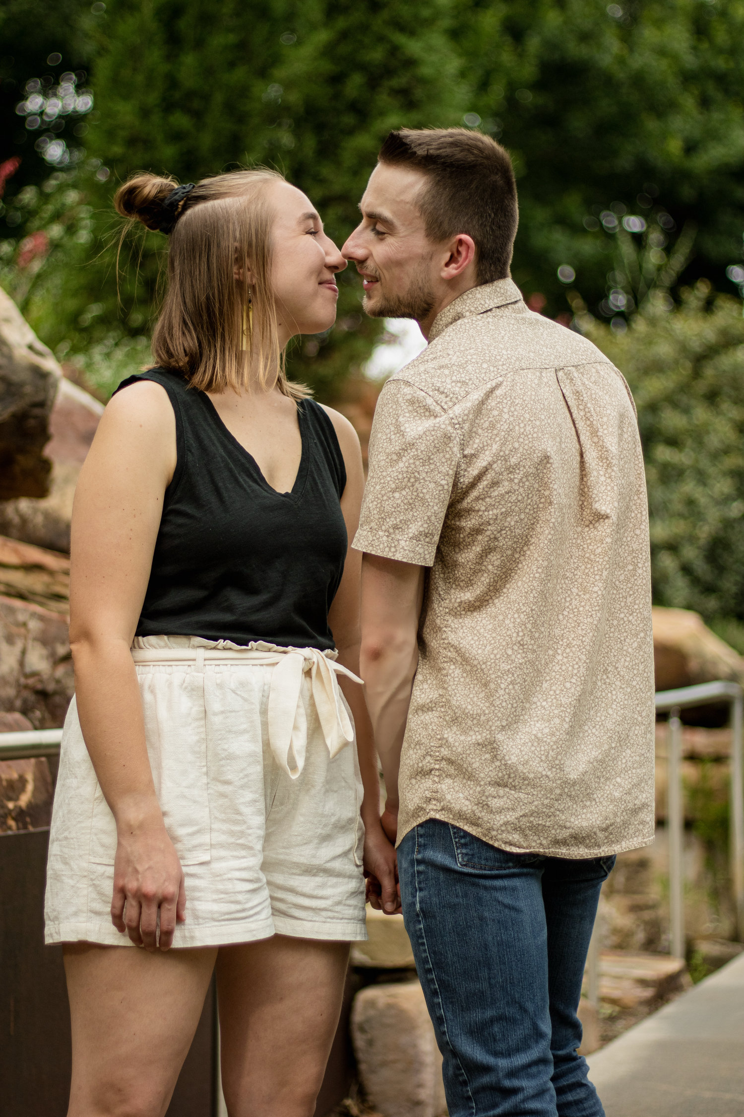 A romantic moment captured in nature as a couple in coordinating outfits share an intimate embrace on a walkway.