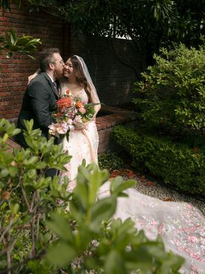 A romantic moment captured in a garden setting with brick walls and scattered rose petals creating a dreamy atmosphere.