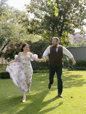 A couple dances playfully on a sunlit lawn, showing off graceful spins and movements in their wedding attire.