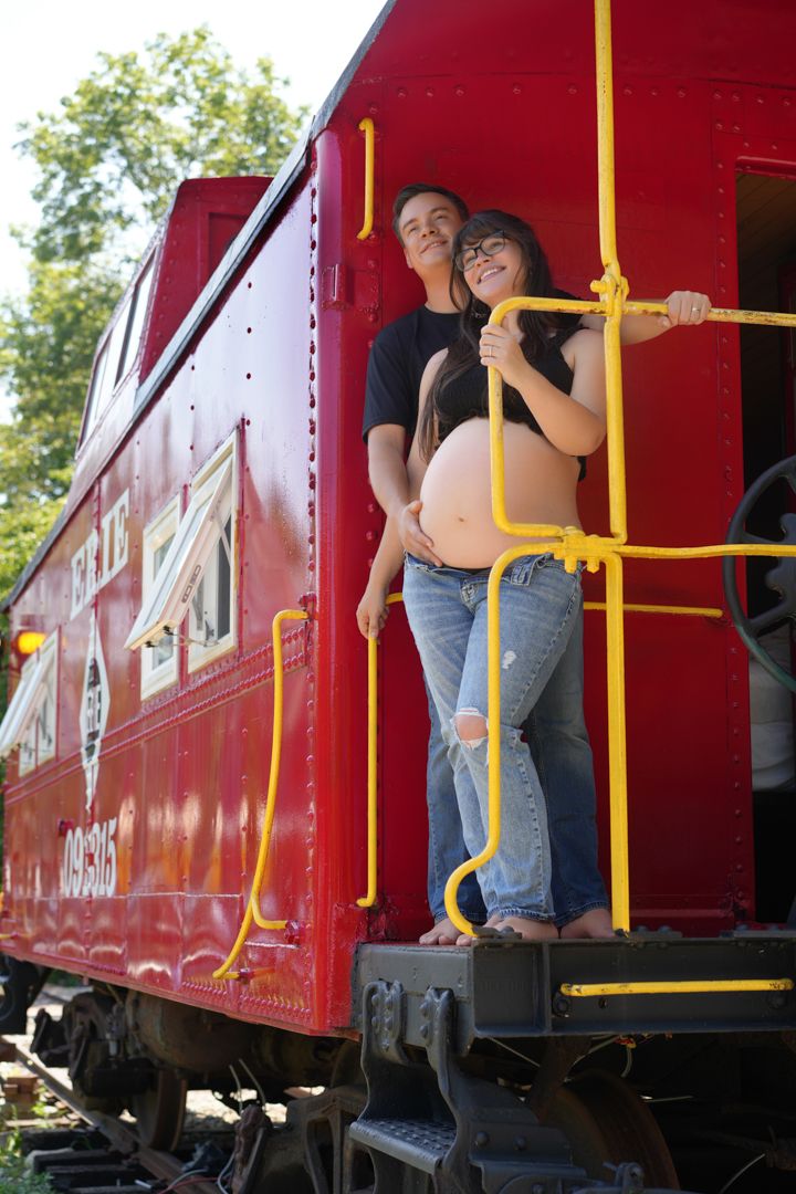 Person stepping onto a vintage red railway car using yellow handrails on a sunny day.