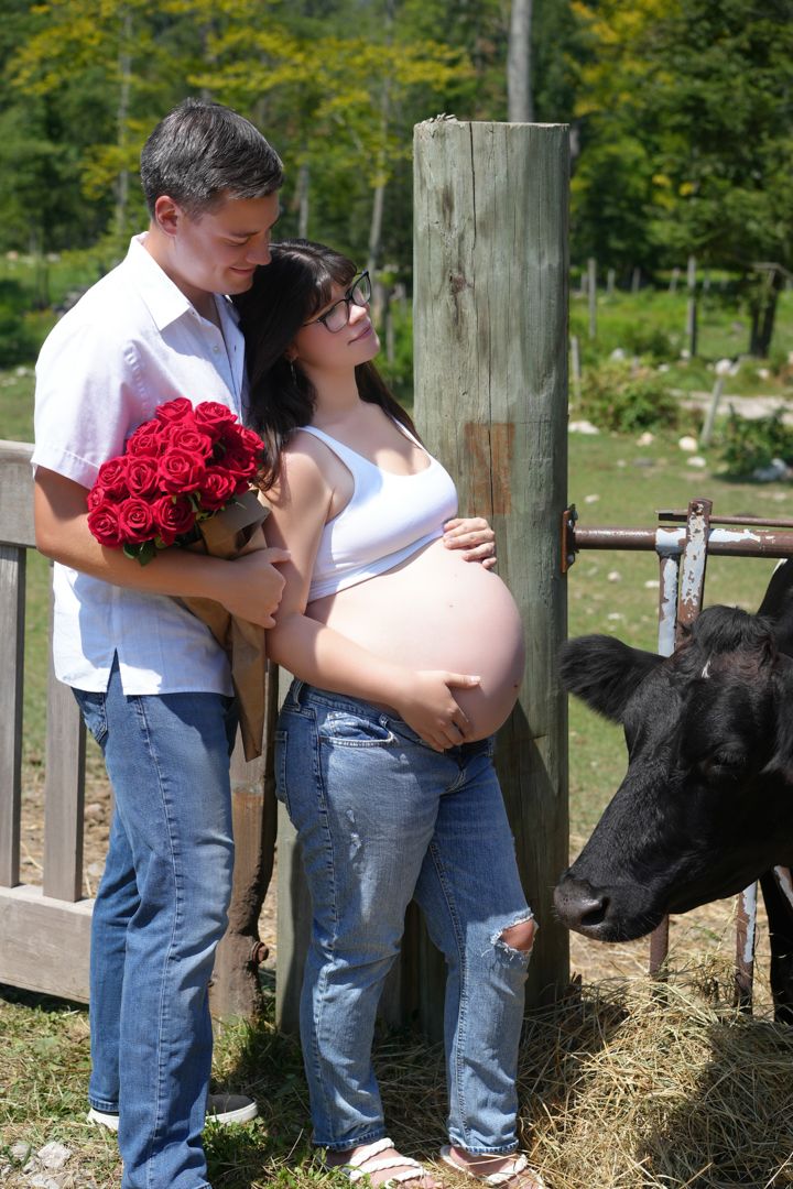 A maternity photo series with a couple embracing near a rustic fence with red roses.