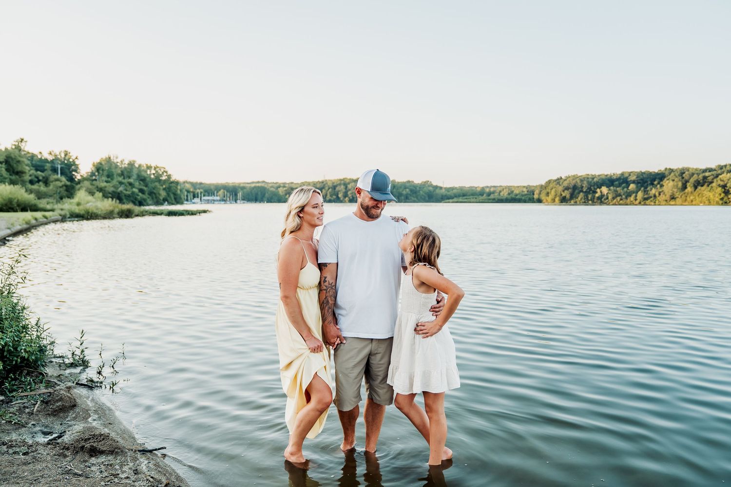 People standing by a tranquil lake during sunset with serene water and lush greenery in the background.