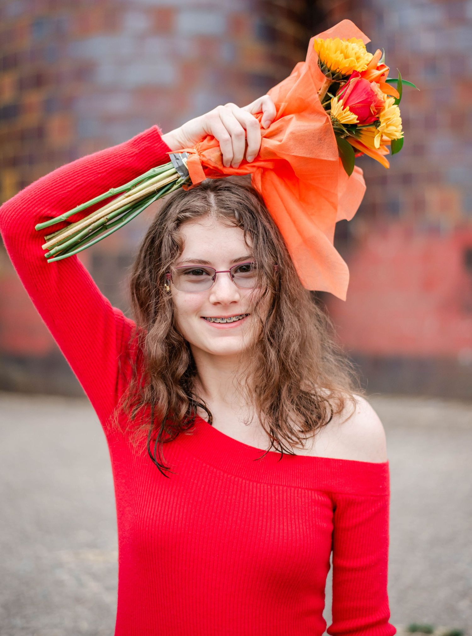 A sequence of four photos showing someone in a bright red sweater playfully posing with orange flowers against a brick wall.