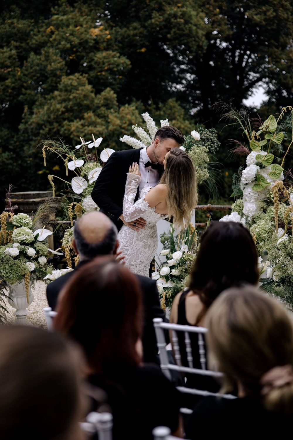 A romantic outdoor wedding ceremony with elegant white floral arrangements and greenery decorating the altar space.