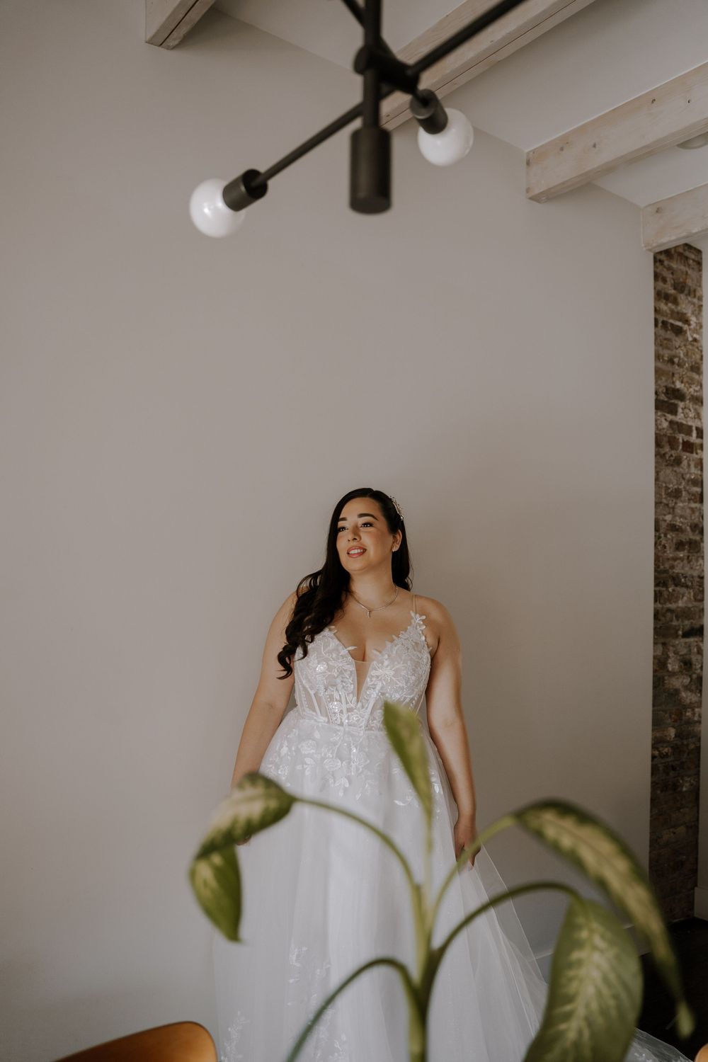A person in a white wedding dress stands in a minimalist room with white walls and track lighting.