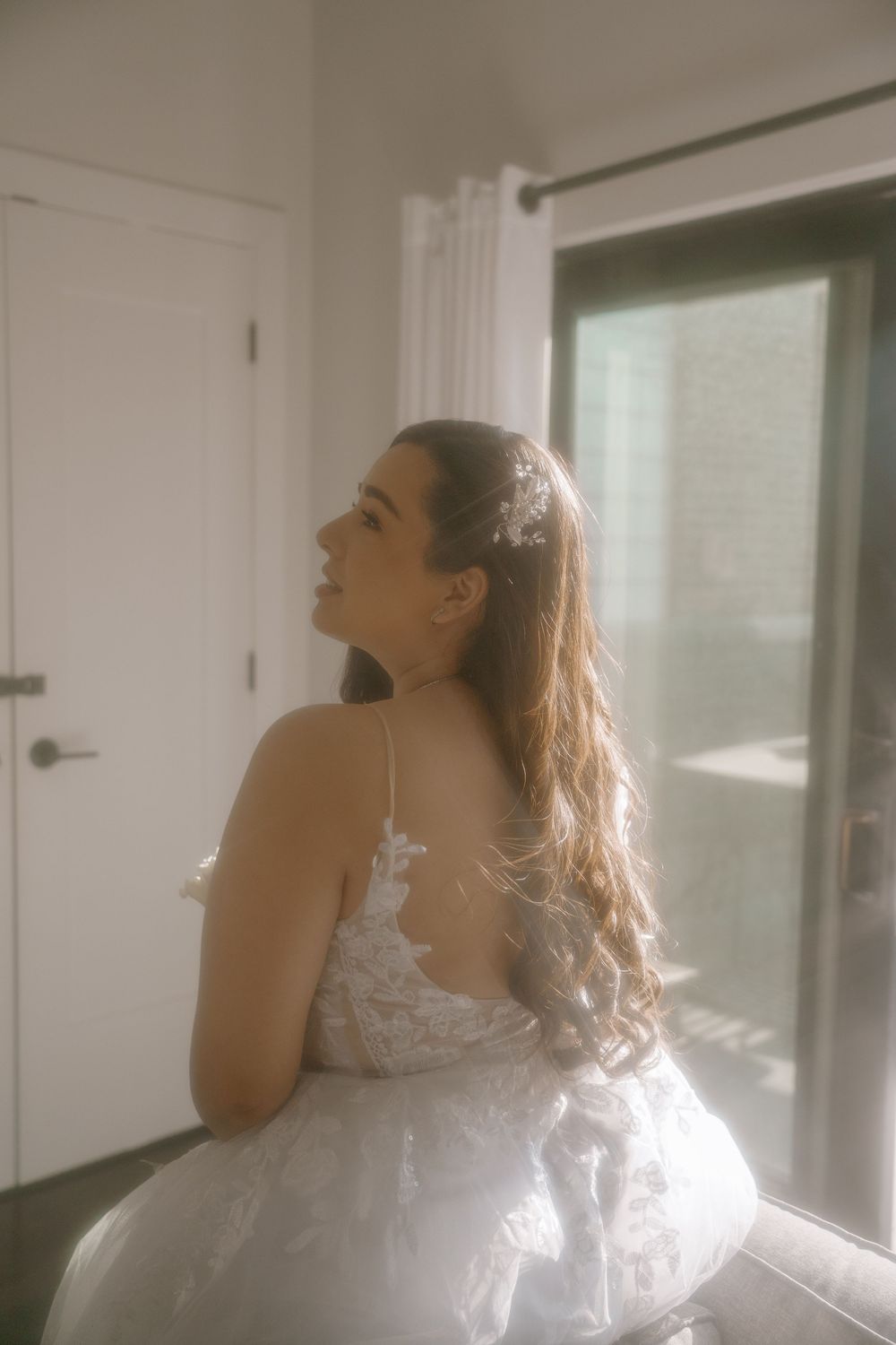 A person in a white lace dress stands near a window with soft sunlight streaming in, creating a dreamy atmosphere.
