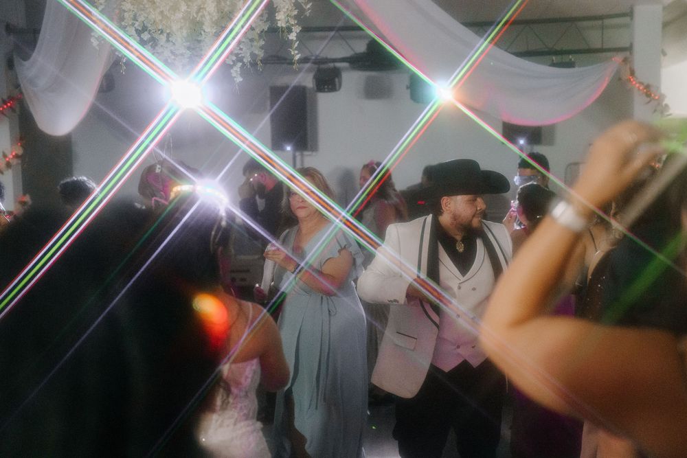 People dance and celebrate at a crowded party with bright flashing lights in a dimly lit room.