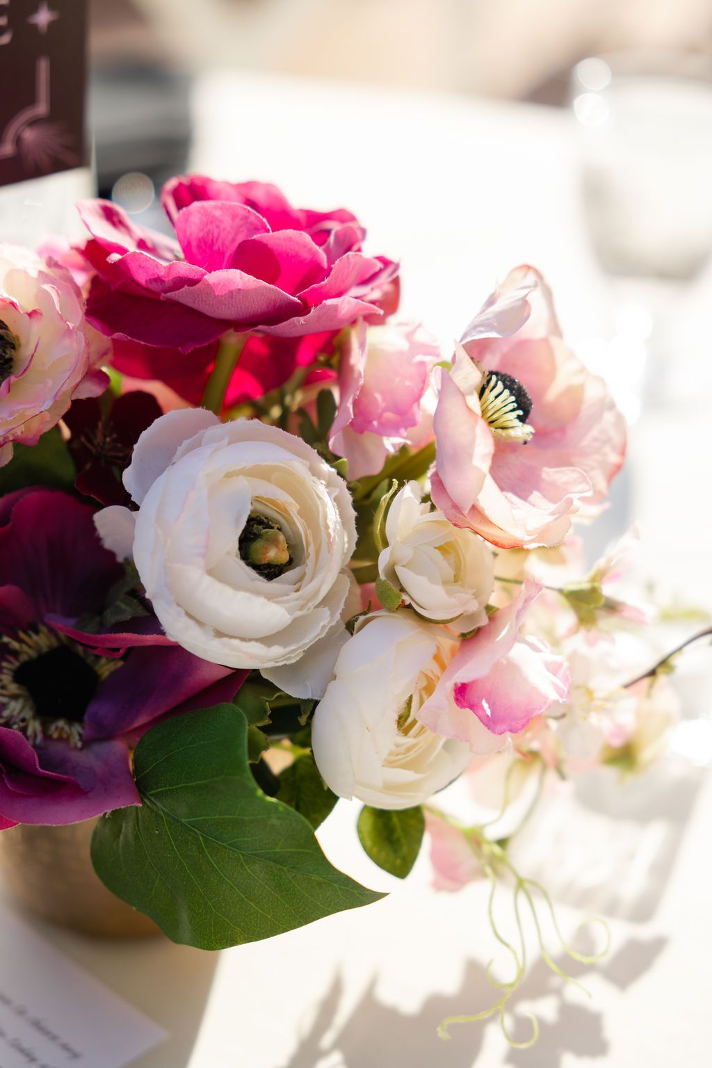 Elegant wedding reception table settings with string lights overhead and pink and burgundy floral centerpieces.