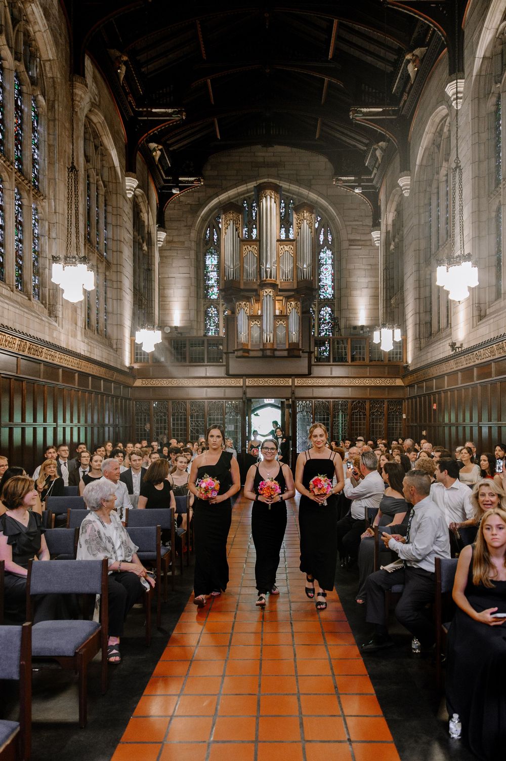 Wedding ceremony taking place in a grand church hall with dark wood paneling and stained glass windows.