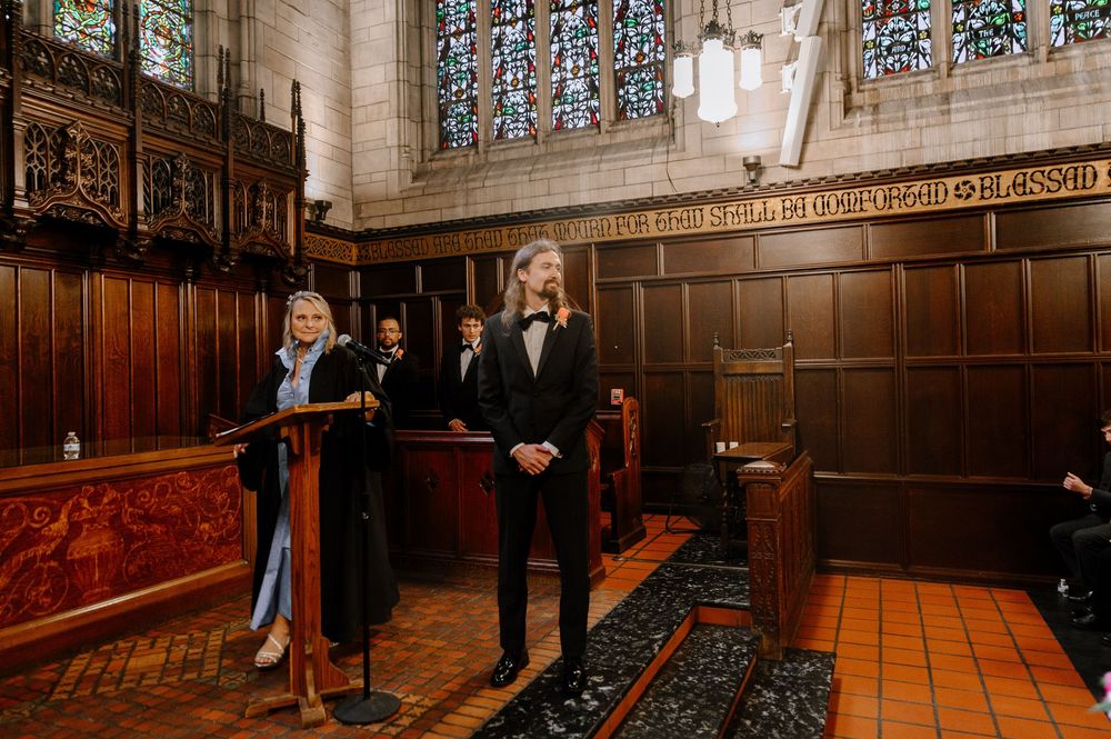 Wedding party stands in historic wood-paneled church sanctuary with ornate stained glass windows and traditional architecture.