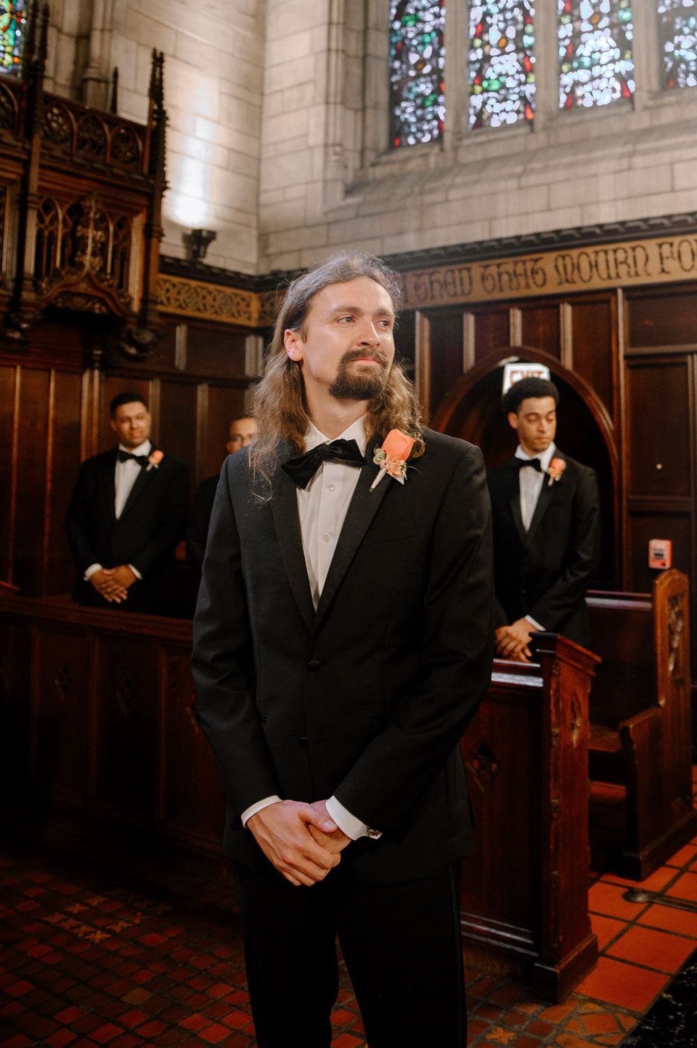 Wedding party members in formal black attire standing inside an ornate church with stained glass windows.