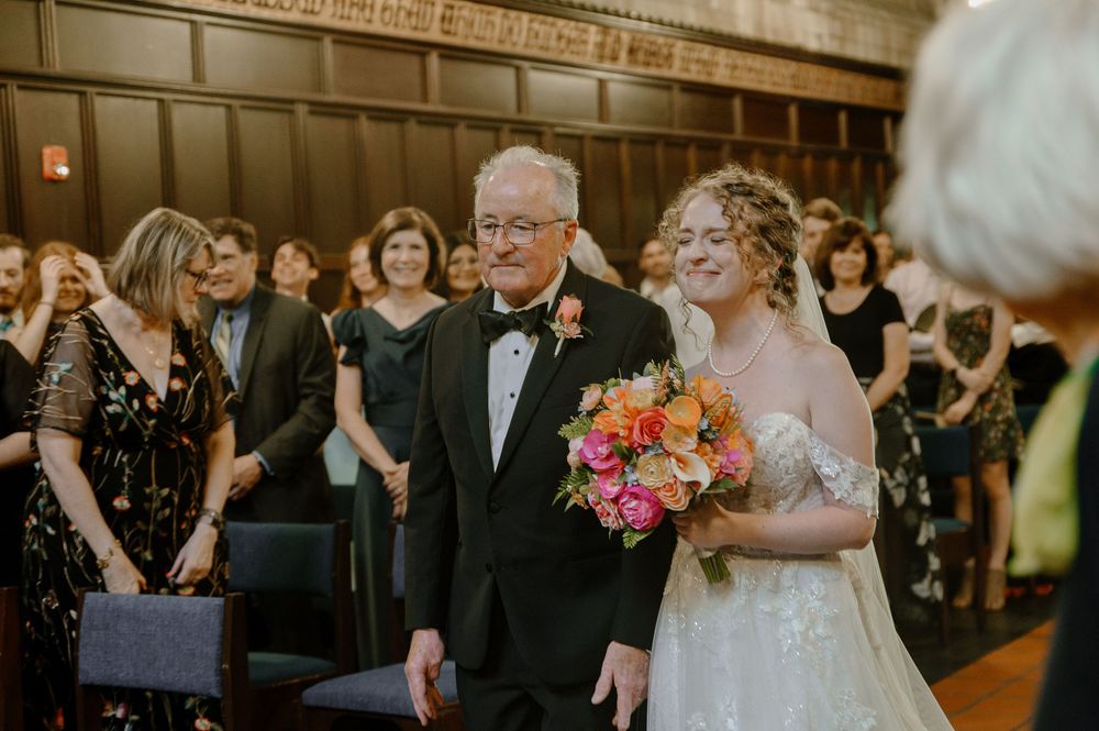 Wedding party walks down the aisle in a cathedral-style church with stained glass windows and wooden pews.