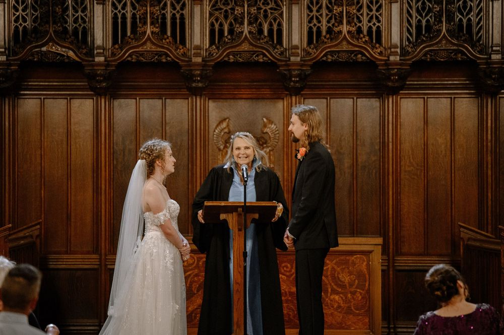 Gothic church interior with ornate wood paneling and stained glass windows during a ceremony.