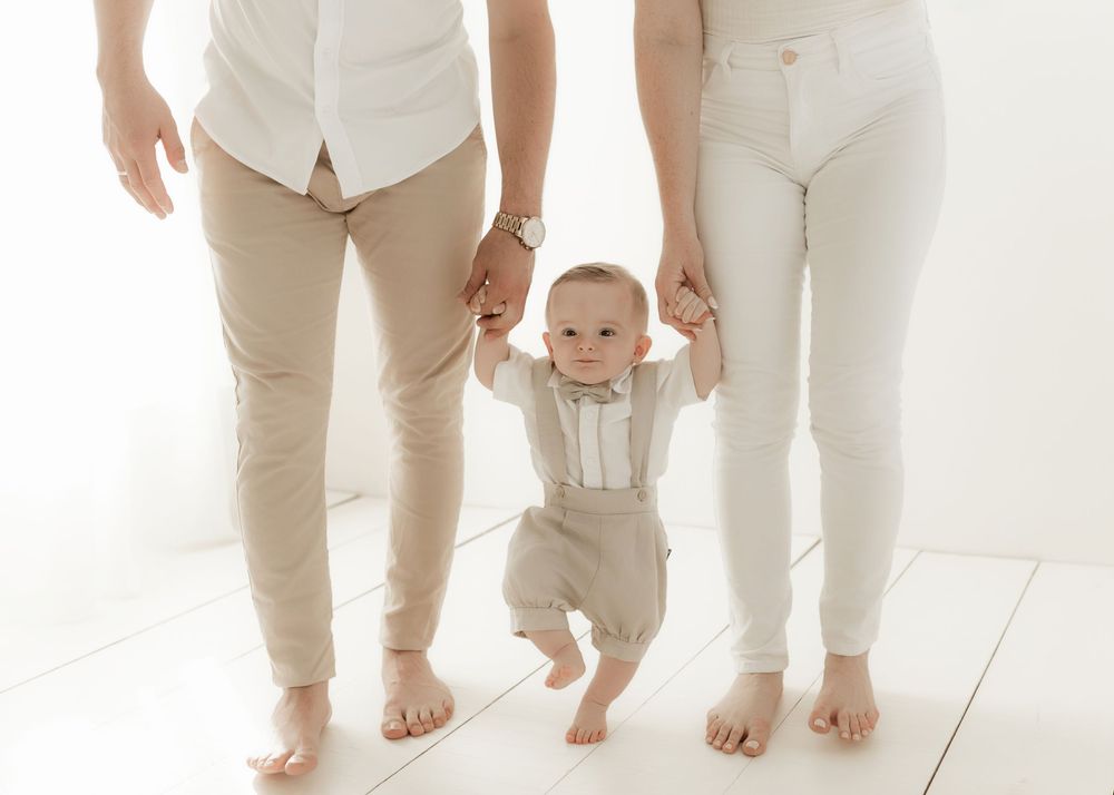 Family members wearing coordinated beige and white outfits stand together showing only their legs and feet on white floor.