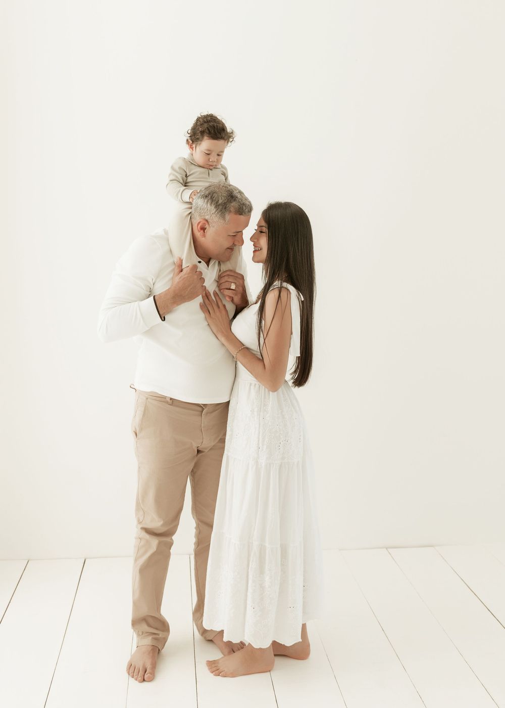 Two people share an intimate moment in white and beige outfits against a minimalist white backdrop.