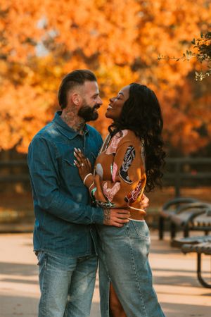 Happy interracial couple laughing and embracing outdoors with vibrant autumn foliage in the background at sunset.